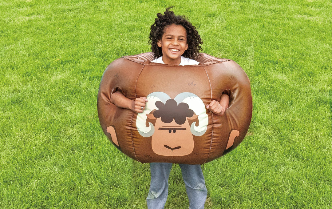 Child smiling and wearing brown Rovers blow-up bumper ball with cartoon ram design on green grass outdoors
