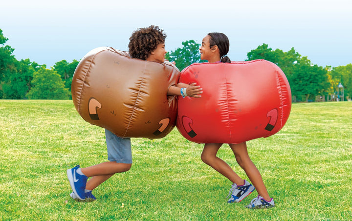 Two children playing outdoors wearing brown and red Rovers blow-up bumper balls on green grass